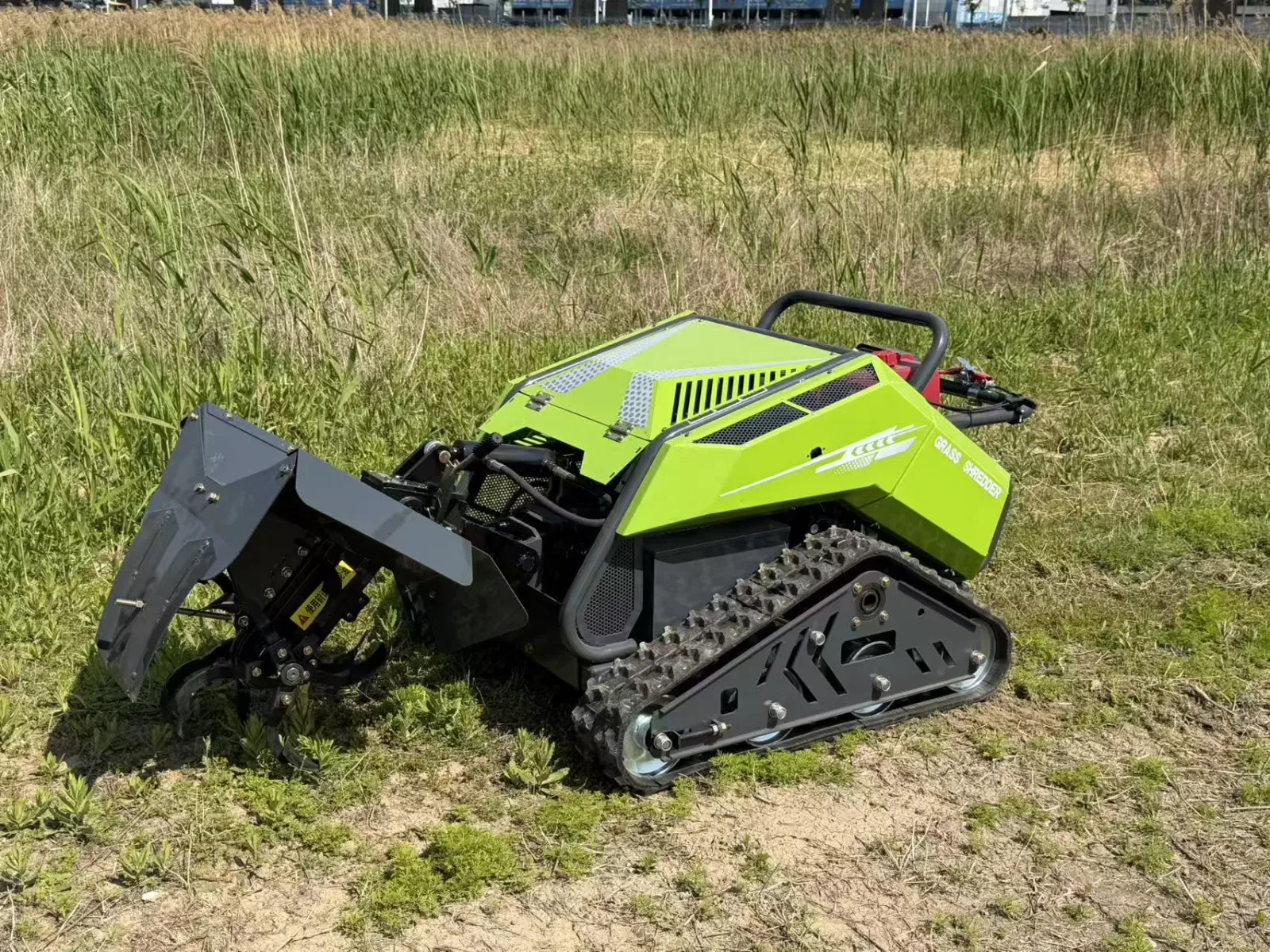 Green tracked mower working at the edge of tall grass