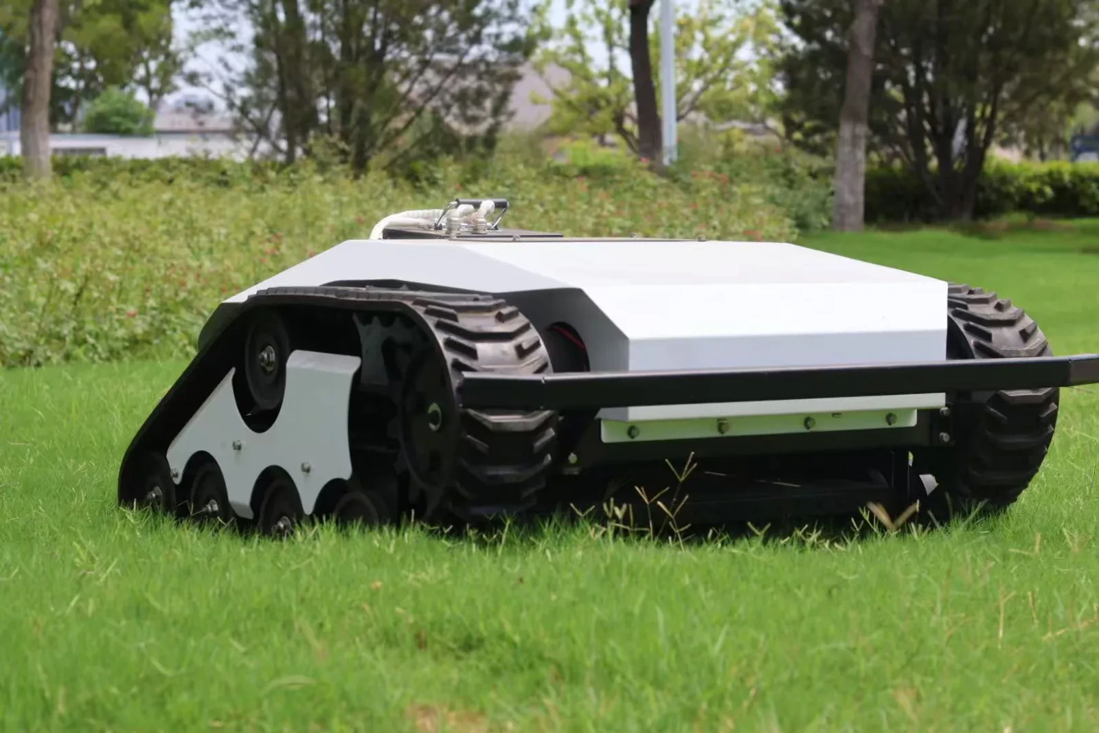 White tracked remote mower photographed at grass level
