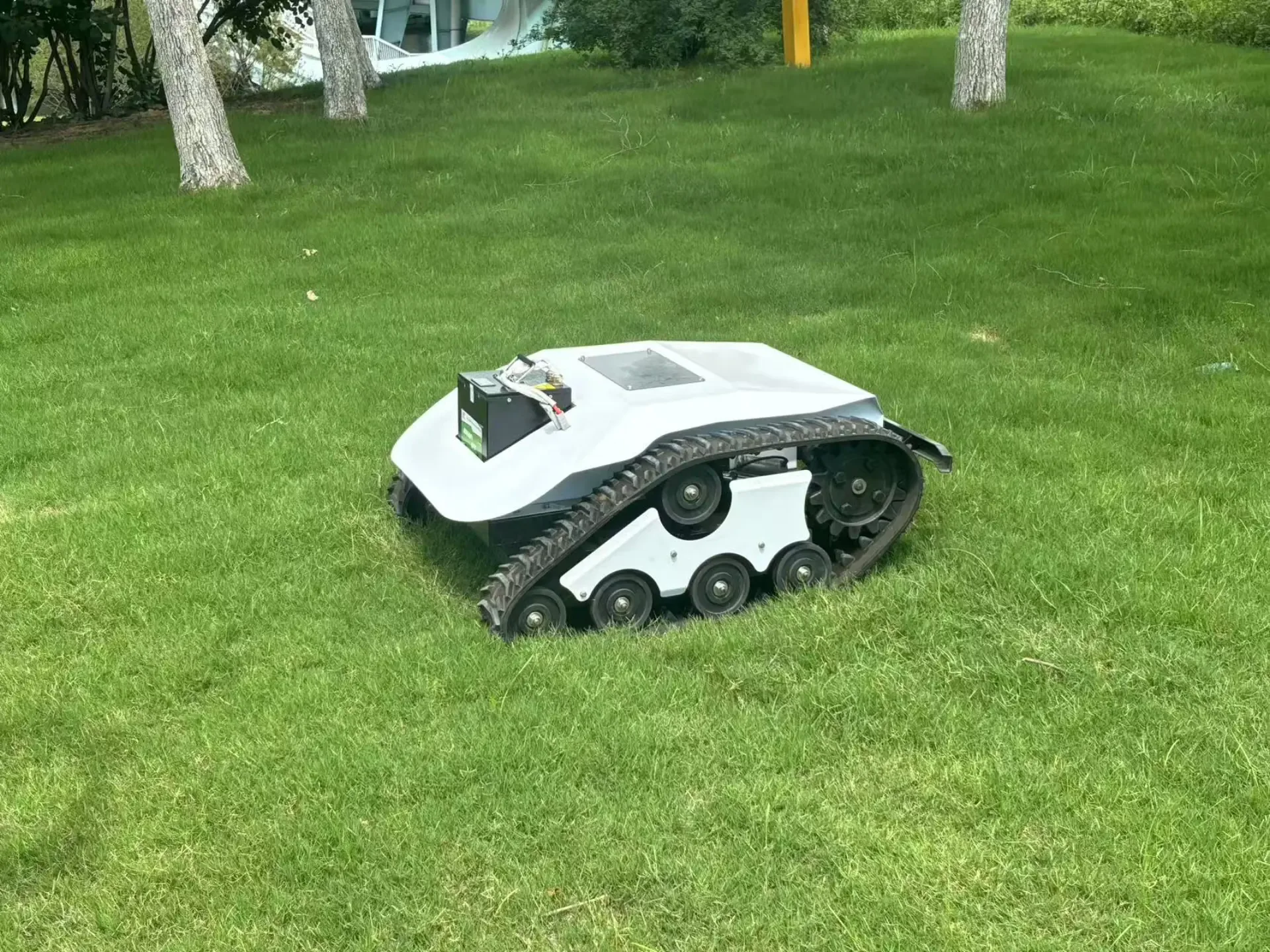 A tracked remote-control mower working on a grassed slope