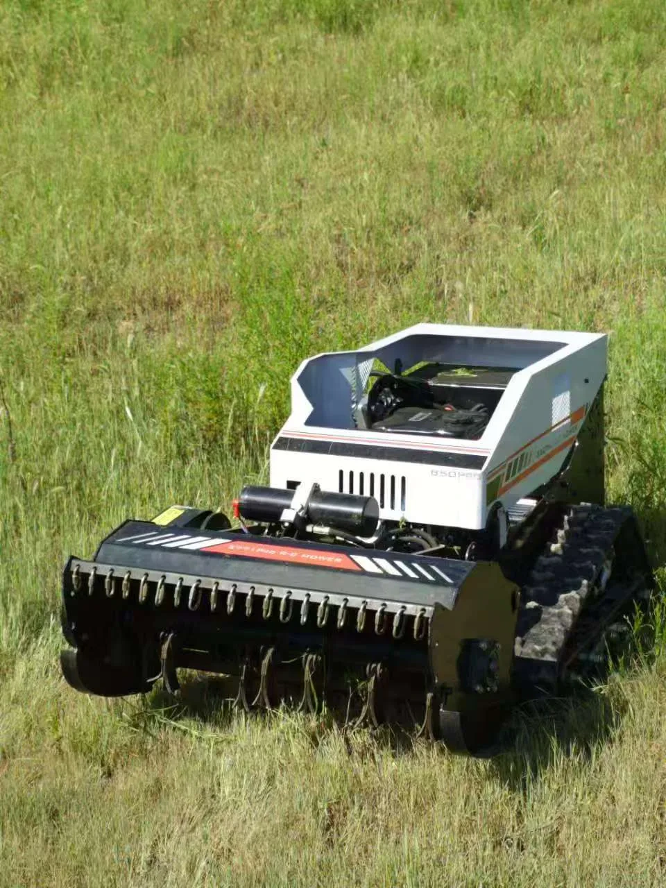 White tracked flail mower moving through tall grass in an outdoor field